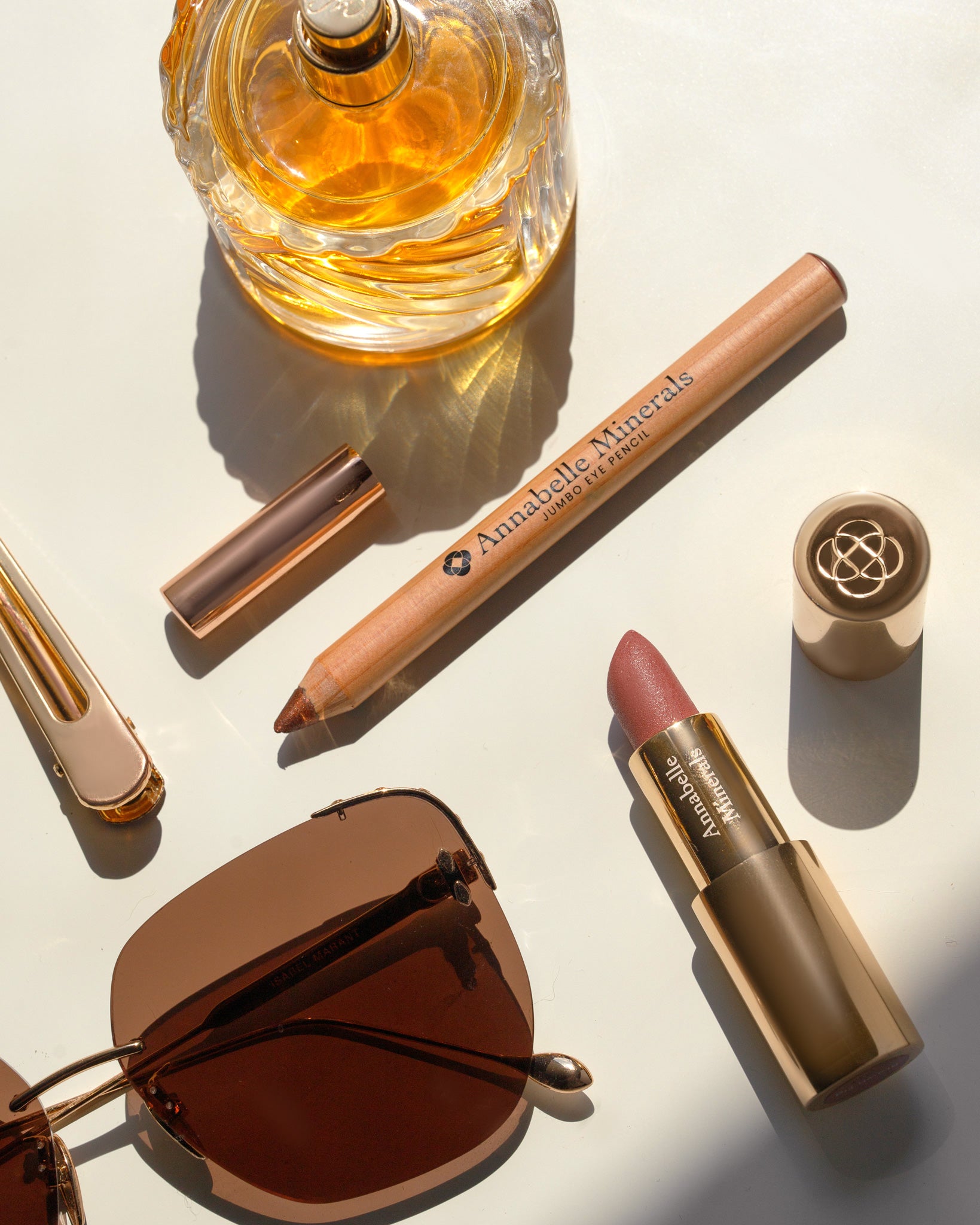 Eleganckie produkty kosmetyczne: perfumy, szminka, kredka do makijażu i okulary przeciwsłoneczne na jasnym tle